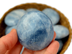 One blue calcite palm stone on hand with some crystals inside a basket