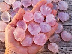 Some pink quartz crystals on hand with background with several crystals on wood table