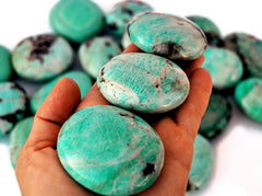 Three amazonite palm stones 60mm-40mm on hand with background with some stones on white 