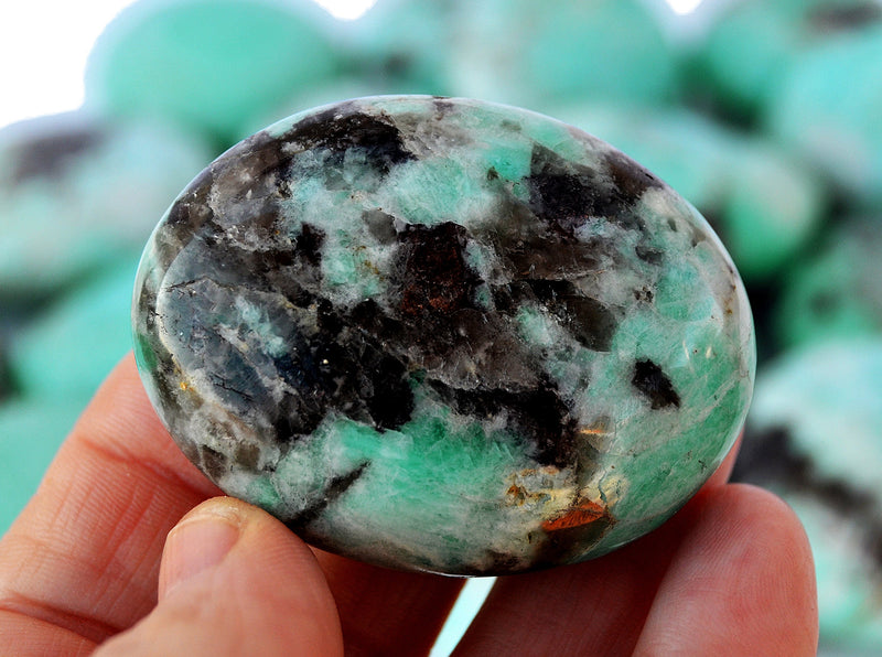 One green amazonite palm stone 50mm on hand with background with some crystals