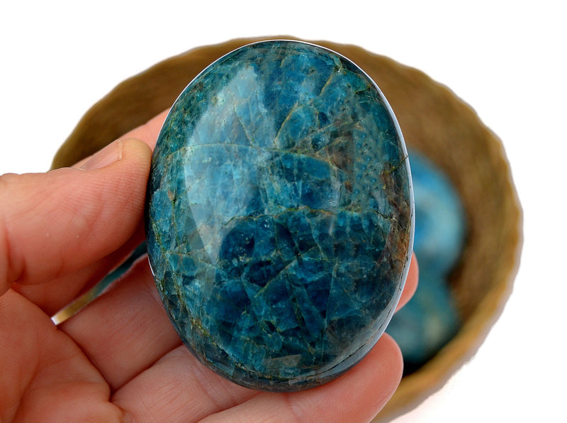 One large blue apatite palm stones 70mm on hand with background with some crystals inside a basket