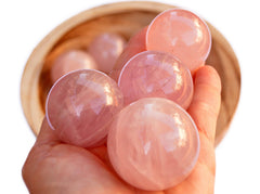 Four rose quartz crystal spheres 40mm on hand with background with several crystals inside a bowl