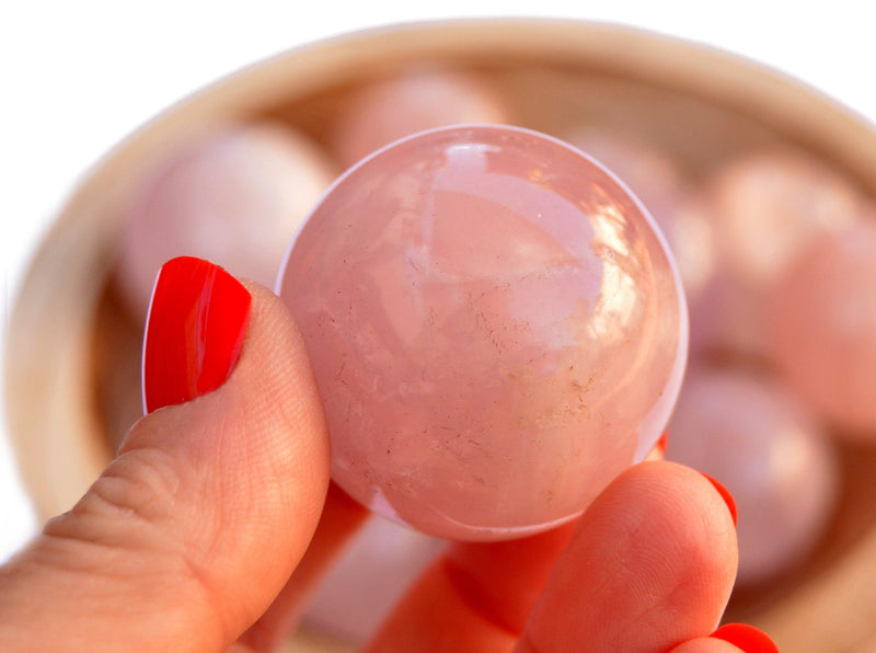 One rose quartz crystal sphere 30mm on hand with background with several crystals inside a basket