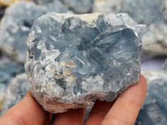 One large blue celestite crystal cluster 80mm on hand with background with some stones