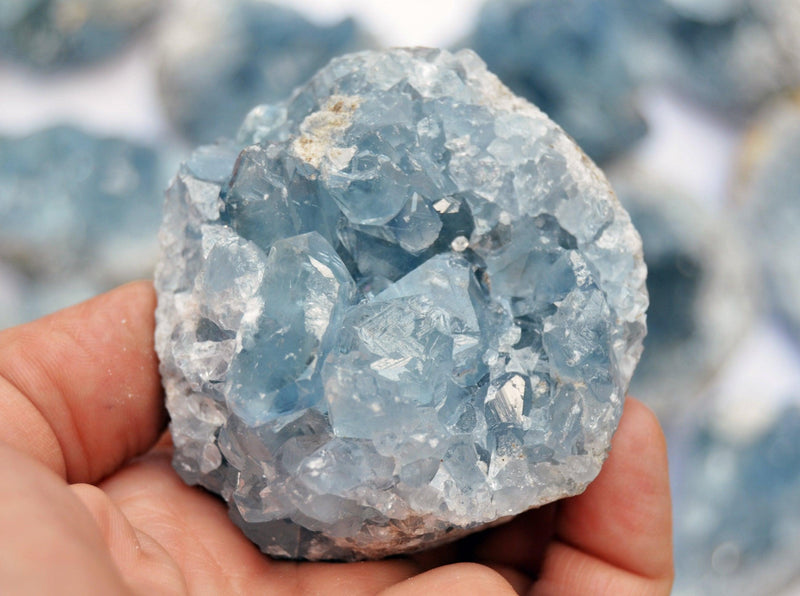 Chunky blue celestite crystal cluster 70mm on hand with background with some stones