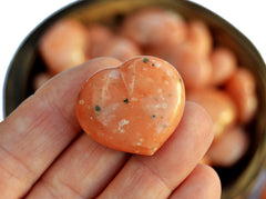 One orange calcite heart stone 30mm on hand with background with several crystals inside a bowl