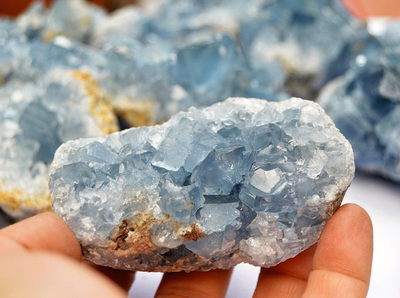 Blue celcestite crystal cluster 70mm on hand with background with some crystals