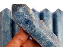 One large blue calcite crystal tower 110mm on hand with background with some stones