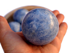 One blue calcite crystal ball 60mm on hand with background with some crystals inside a wood bowl