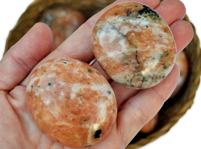 Two orange calcite palm stones on hand with background with some crystals inside a basket