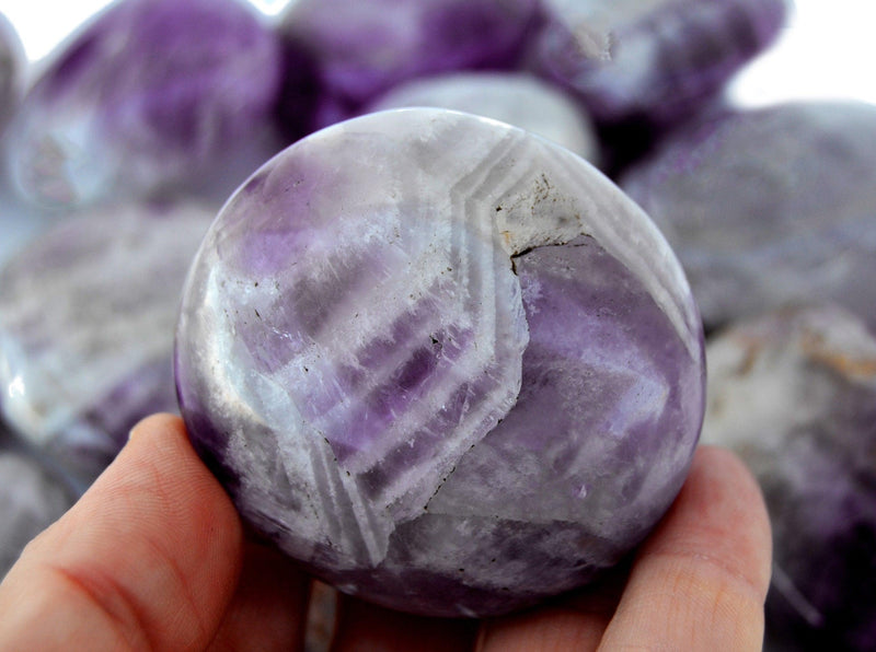 One amethyst palm stone 60mm on hand with background with several crystals