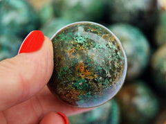 Green chrysocolla sphere crystal 30mm on hand with background with several spheres