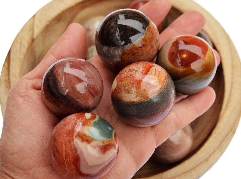 Five polychrome multicolor jasper sphere crystals 25mm - 40mm on hand  with background with some spheres inside a wood bowl