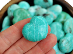 One amazonite crystal heart 30mm on hand with background with several crystals inside a bowl