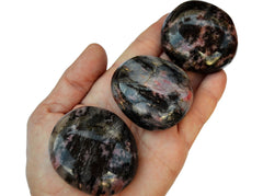 Three rhodonite palm stone crystals on hand