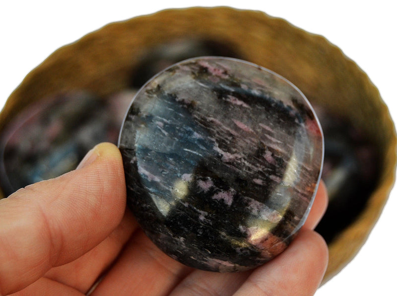 One rhodonite palm stone 60mm on hand with background with some crystals inside a basket