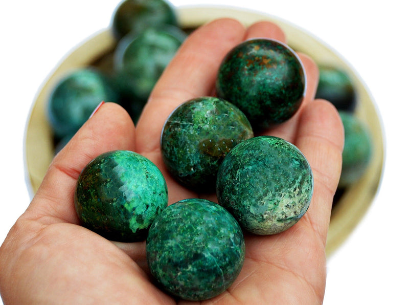 Several green chrysocolla sphere stones 25mm - 35mm on hand with background with some balls inside a wood bowl
