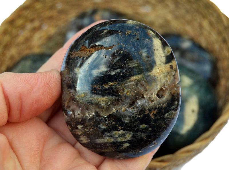 Large sea  jasper palm stone 55mm on hand with background with some stones inside a basket
