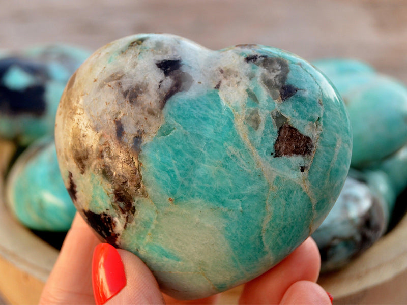 Large green amazonite crystal heart 70mm on hand with background with some stones inside a bowl
