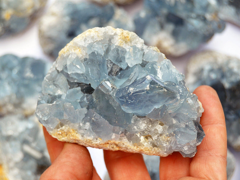 Blue celcestite geode 70mm on hand with background with some crystals