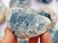 Blue celestite crystal cluster 60mm on hand with background with some crystals 