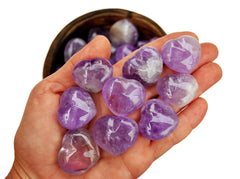 Some small amethyst heart crystals 30mm on hand with background with some hearts inside a bowl
