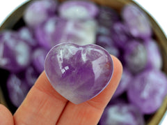 One small amethyst puffy heart crystal 30mm on hand with background with several hearts inside a bowl