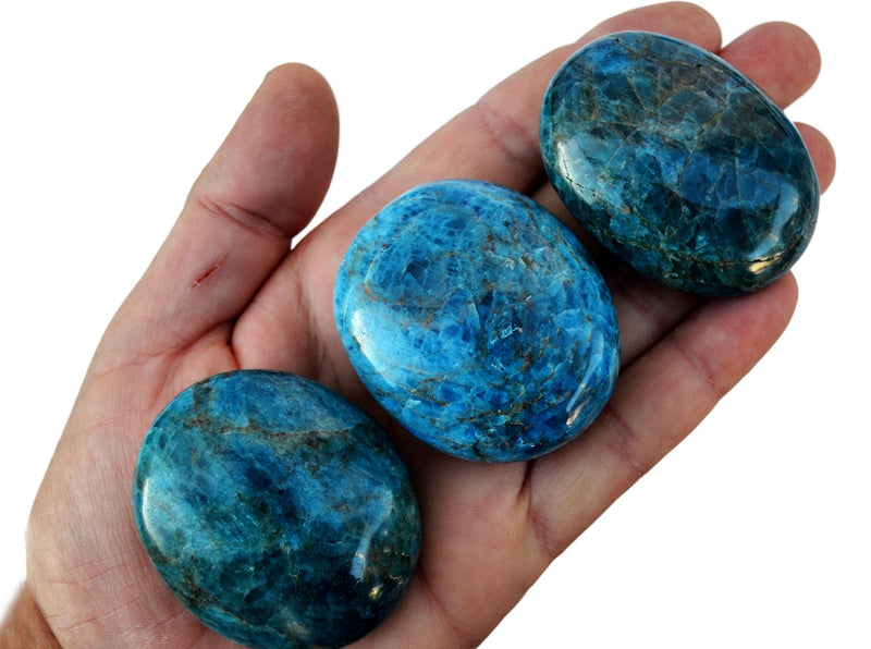 Three blue apatite palm stones 45mm on hand with background with some crystals on white