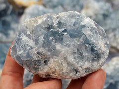 Chunky blue celestite crystal cluster 80mm on hand with background with some stones