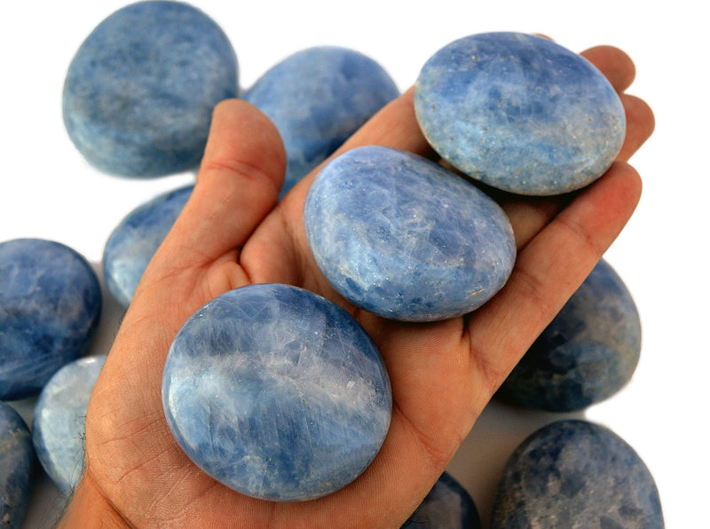 Three blue calcite palm stones on hand with background with some crystals