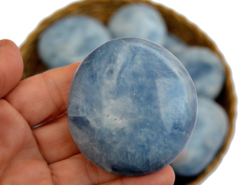 One large blue calcite palm stone on hand with some crystals inside a basket