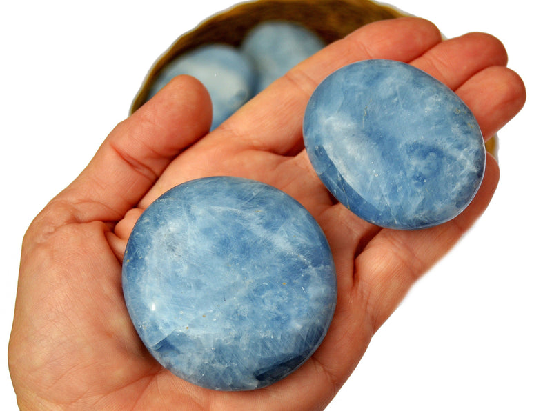 Two blue calcite palm stone crystals  on hand with background with some crystals