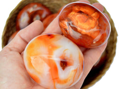 Two natural carnelian palm stones 60mm-70mm on had with background with some stones inside a basket on white