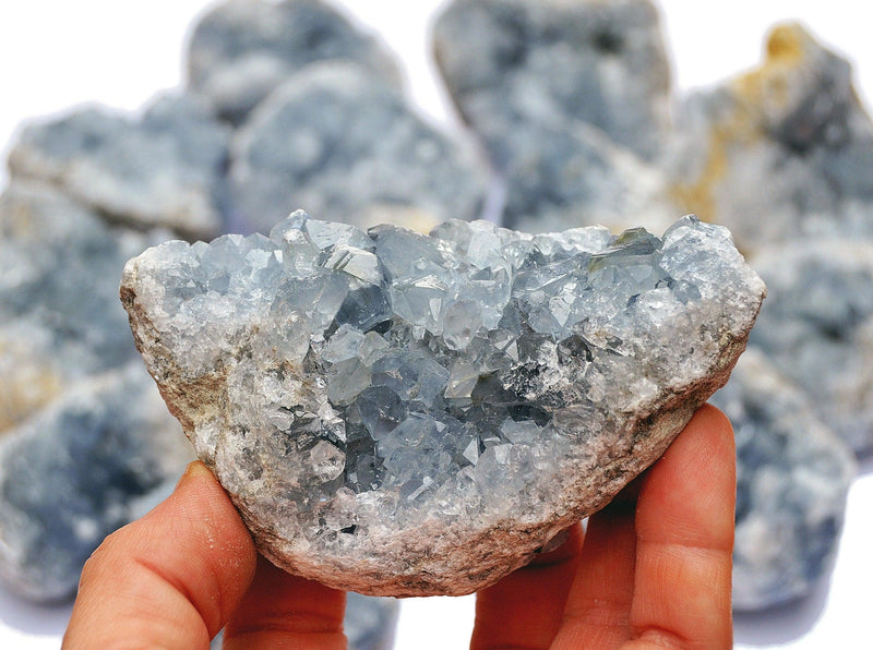 One blue celestite crystal cluster 70mm on hand with background with several stones 