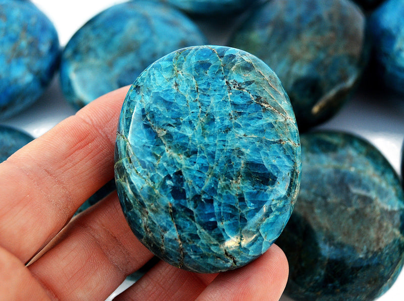 On blue apatite palm stone crystal 50mm on hand with background with some stones on white