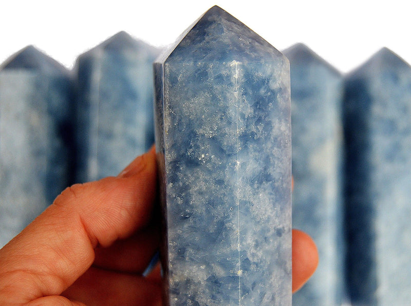 One big blue calcite crystal tower 110mm on hand with background with some stones