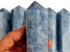 One chunky blue calcite crystal point 110mm on hand with background with some towers on hand