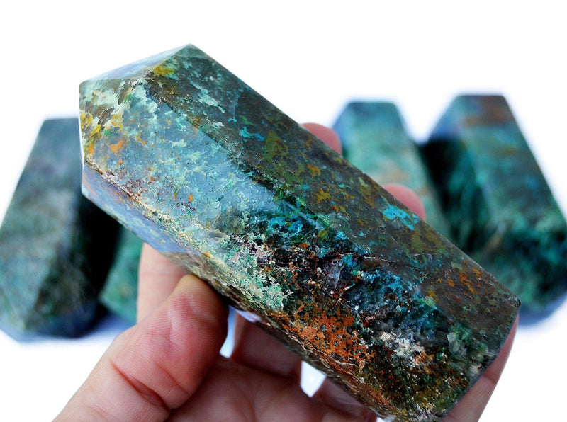 One large green chrysocolla obelisk 110mm on hand with background with some stones