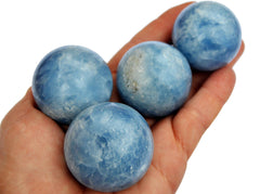 Four blue calcite sphere crystals 25mm-40mm on hand with white background
