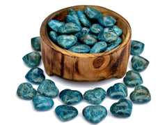 Several small blue apatite heart carving minerals inside a wood bowl and some crystals outside on white background