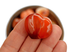 One small carnelian heart crystal 30mm on hand with background with some specimens inside a bowl on white