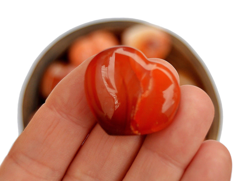 One small carnelian heart stone 30mm on hand with background with some hearts inside a bowl
