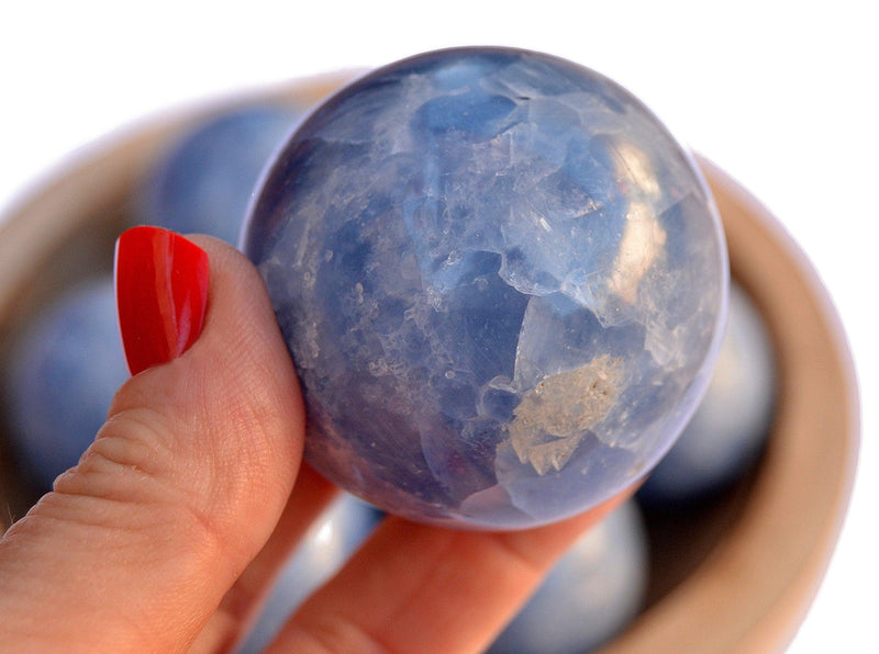 One blue calcite sphere mineral 50mm on hand with background with some balls inside a wood bowl