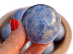 One blue calcite crystal ball 55mm on hand with background with some crystals inside a wood bowl