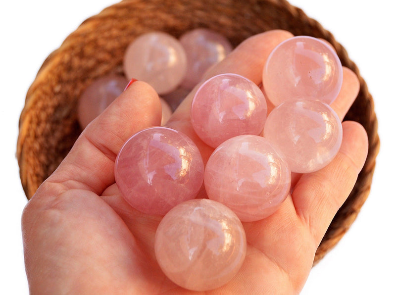 Some pink quartz crystal balls  30mm on hand with background with several crystals inside a basket