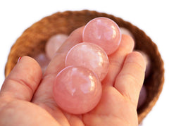 Three pink quartz crystal balls 40mm on hand with background with several crystals inside a basket