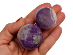 Two purple amethyst crystal spheres on hand with white background