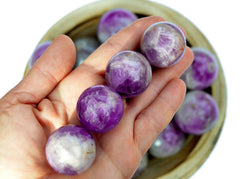 Four amethyst crystal spheres on hand with background with several stones inside a bowl