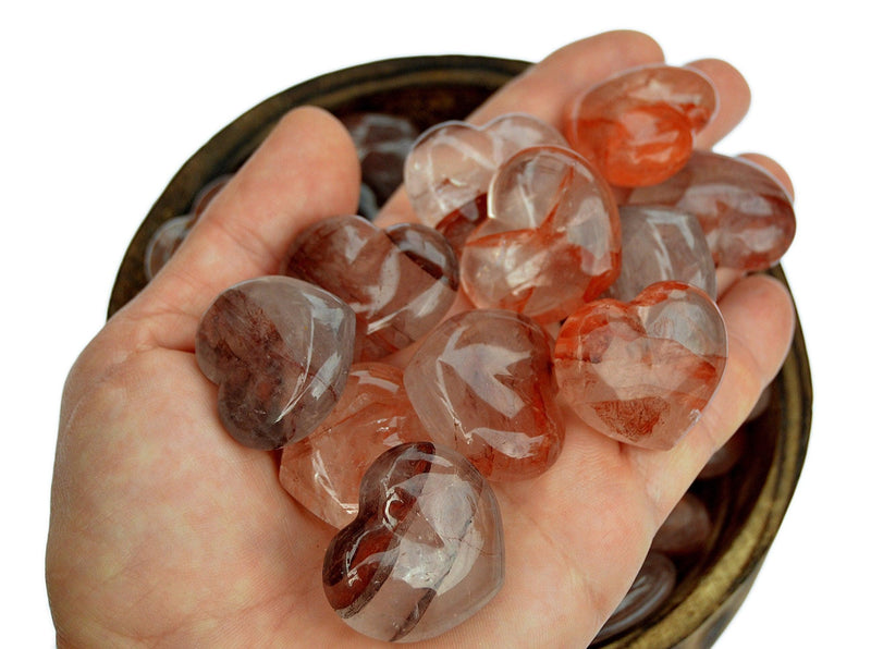 Some fire quartz heart crystals 30mm on hand with background with some stones insde a bowl
