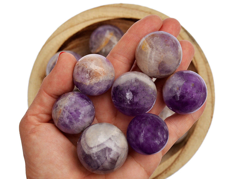 Seven amethyst crystal spheres on hand with background with some stones inside a bowl